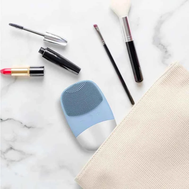 Brosse nettoyante sonique bleue avec accessoires de maquillage sur une surface marbrée
