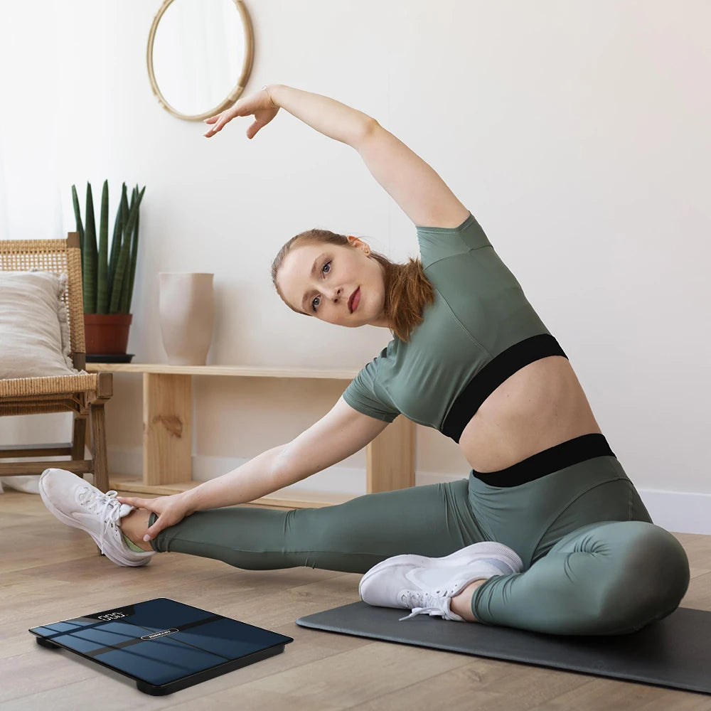 Femme en leggings de sport utilisant un balance impédancemètre connectée lors d'une séance d'étirement