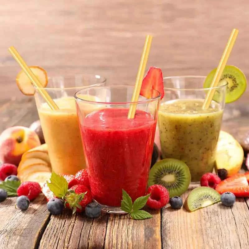Trois smoothies colorés avec des pailles en bambou écologiques sur une table en bois