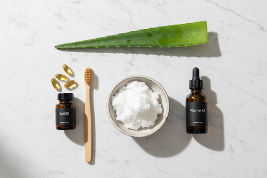 Routine de soins naturels pour la parodontite, montrant de l'huile de coco, une brosse en bambou, des vitamines K2 et CoQ10, et de l'aloe vera sur un fond en marbre.